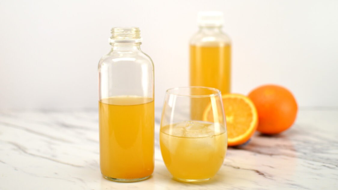 glass and bottle of orange kombucha